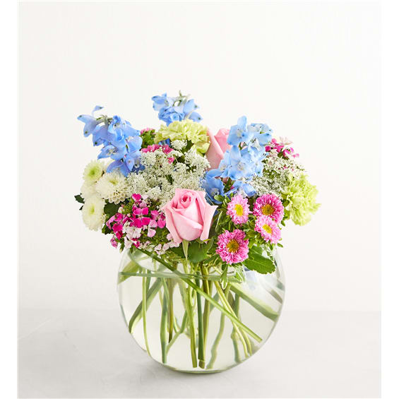 Mixed bouquet of pink, blue, and white flowers in a clear glass vase