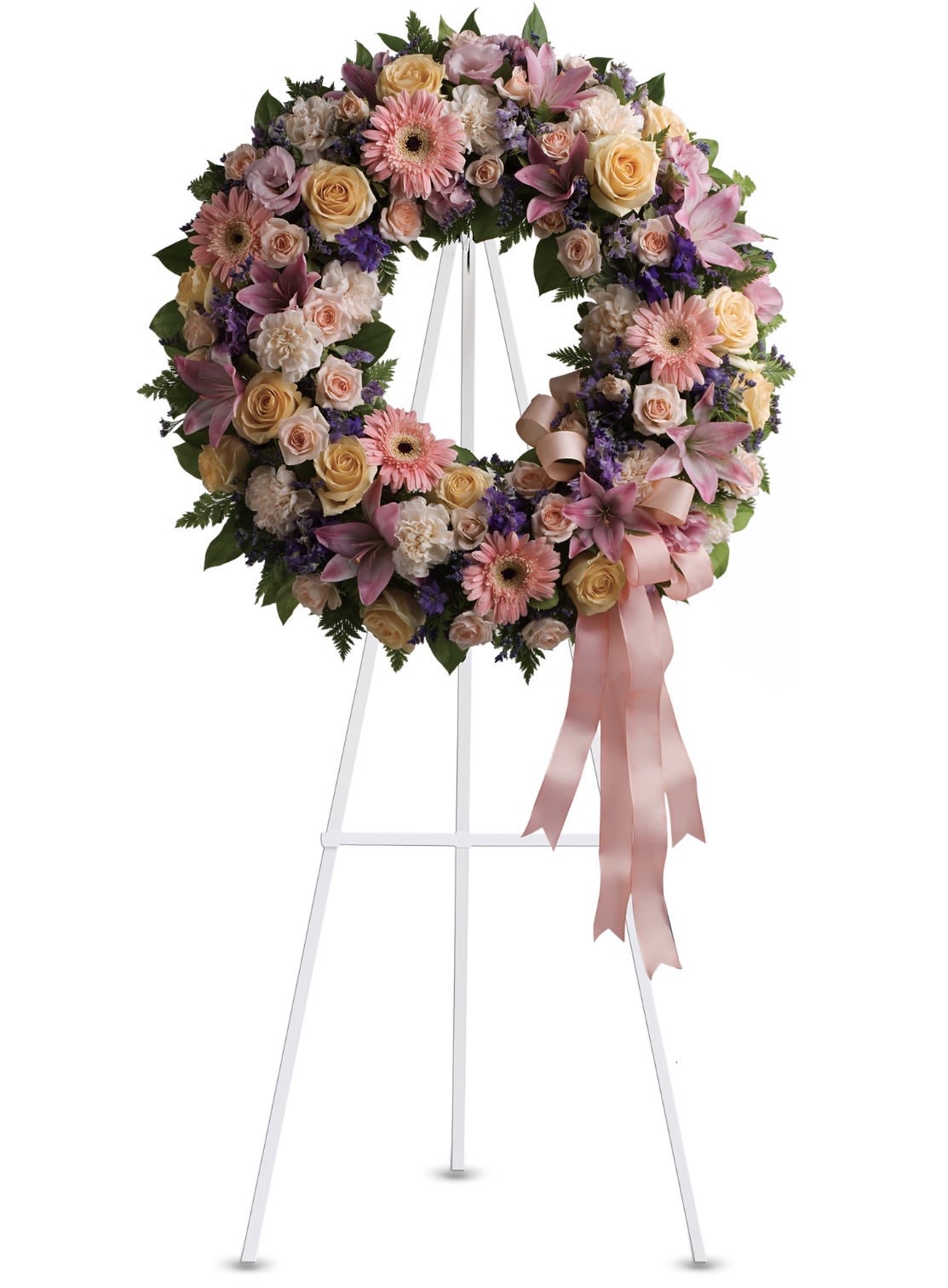 Graceful Wreath - A full, circular sympathy wreath arranged in soft lavender, peach, pink, purple, green, white and yellow tones-designed to speak with quiet grace at a funeral or memorial service. The floral display sits on a white easel and reads as a respectful tribute: the mix of roses, gerbera daisies, carnations and lily-like blossoms creates a gentle, ceremonial presence that comforts the person you're honoring.  The design is densely filled for a lush, rounded silhouette with well-balanced color transitions from cream and peach to lavender and rose. A pink satin ribbon cascades from the lower right, giving a formal finished touch that draws the eye and complements the pastel palette. The wreath's generous proportions make it suitable as a prominent front-of-service tribute or a centerpiece at a graveside gathering.  Made to convey sympathy and remembrance, this arrangement helps the bereaved feel seen and supported during a difficult moment while remaining appropriate for other formal occasions like weddings or commemorative events. Displayed on the included white easel, it arrives ready to present; minimal care is needed beyond keeping it cool and sheltered from direct sun until the service.