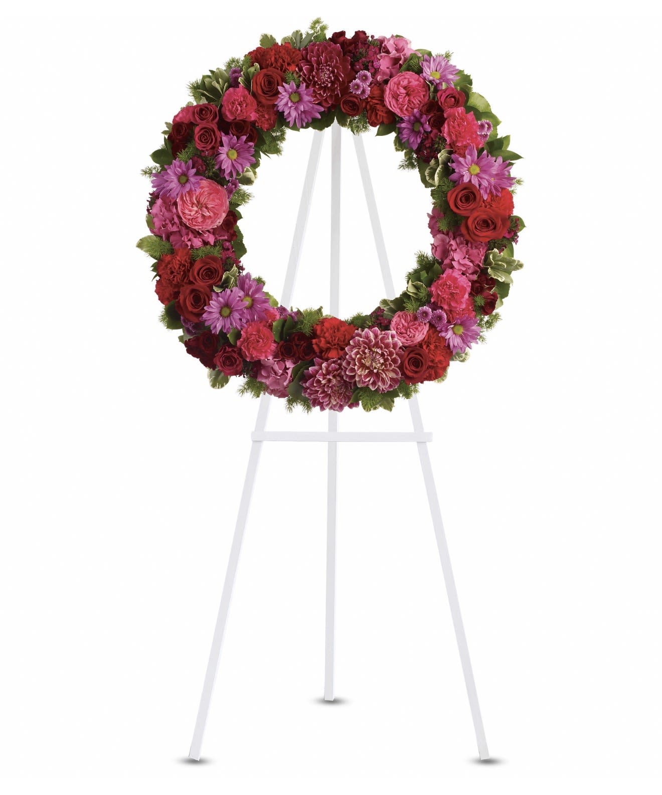 Infinite Love - A lush circular wreath built in a rich palette of pink, red, purple, and green makes an immediate, comforting statement - a sympathy and funeral flower arrangement designed to honor a life with warmth and reverence. The full, continuous ring of blooms mounted on a white easel reads both ceremonial and personal, the kind of tribute that helps the person you're remembering feel genuinely celebrated and deeply missed.  Densely packed roses, spray roses, carnations, chrysanthemums, daisies and hydrangeas create layered texture and saturated color across the wreath, producing a balanced, symmetrical silhouette with an open center. The mix of large focal roses and hydrangea clusters with smaller spray roses and daisy-like flowers gives visual movement and softness; greens tucked through the blooms add calming contrast and natural depth. Finished on a sturdy white easel, the arrangement is sized for a funeral service or memorial display where it will be clearly visible and richly expressive.  Appropriate for a memorial, celebration of life, or any ceremony where a formal, heartfelt tribute is called for, this wreath says "infinite love" without words. If you need delivery to a service or help selecting an accompanying sympathy item, we can assist with timing and placement to ensure the piece arrives ready to honor the occasion.