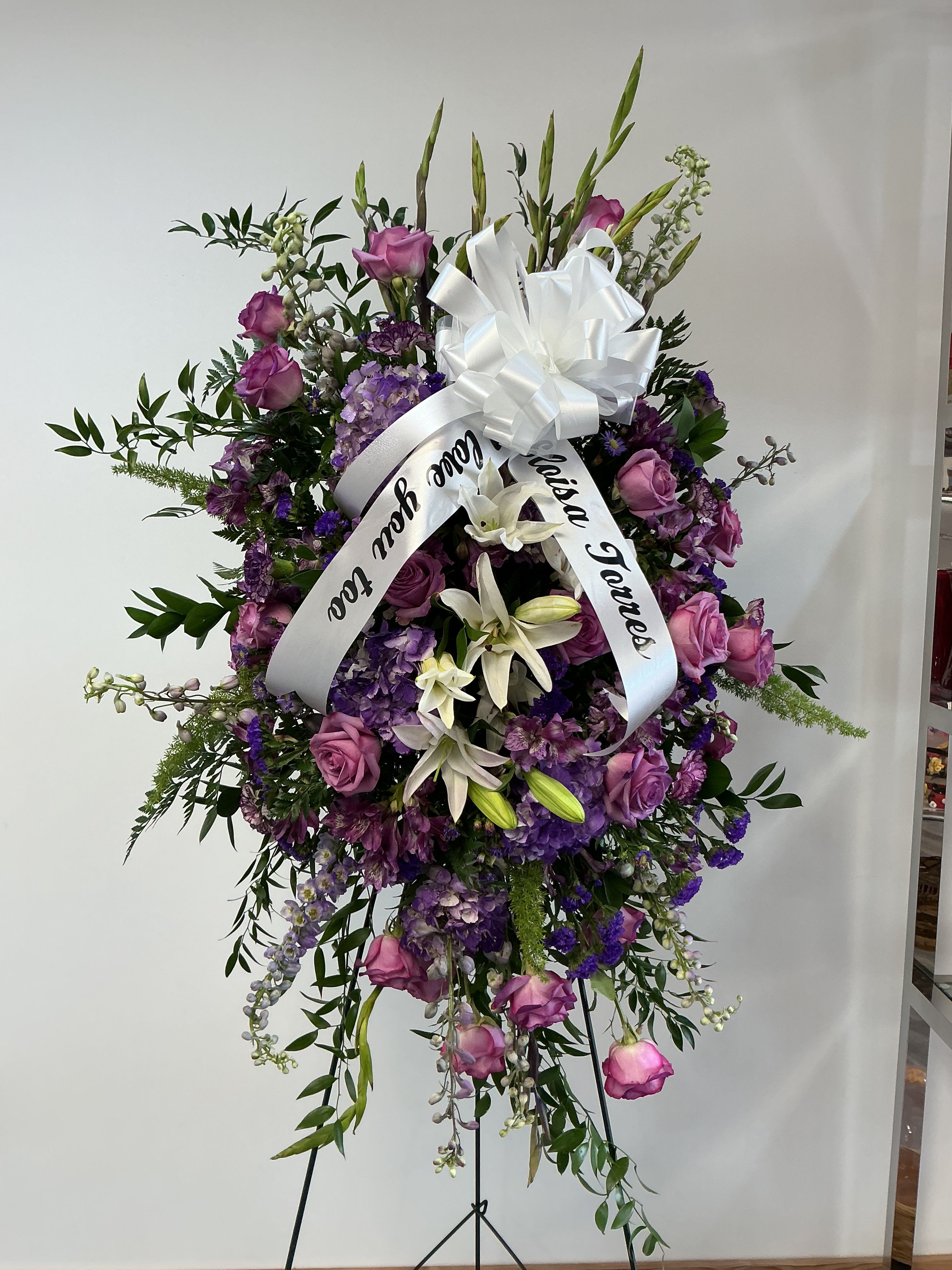 Descanso sereno -   A graceful standing spray of lavender roses, white lilies, and purple blooms, created to honor a loved one’s memory.  