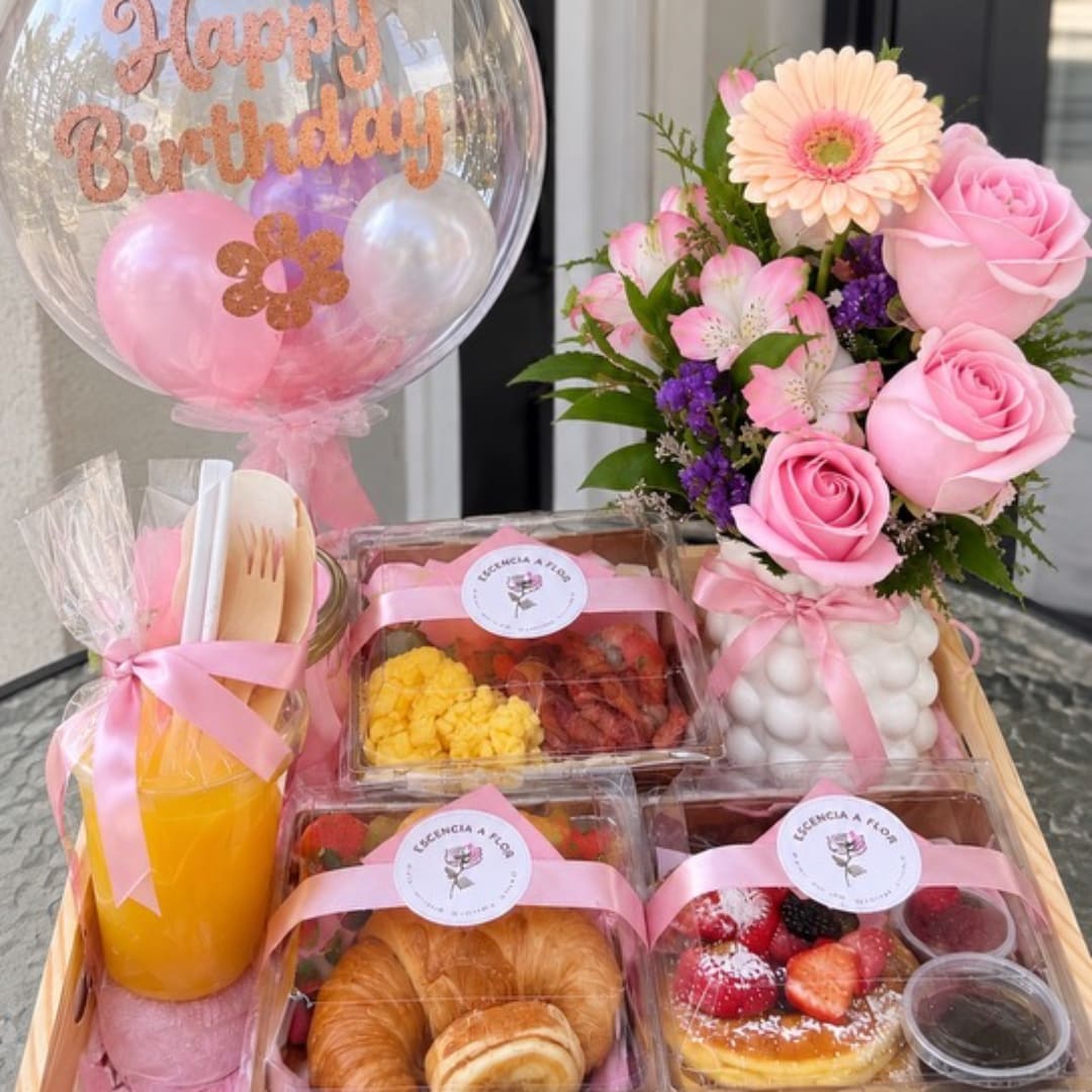 Birthday gift basket with pink roses, a balloon, juice, pastries, and fruit boxes