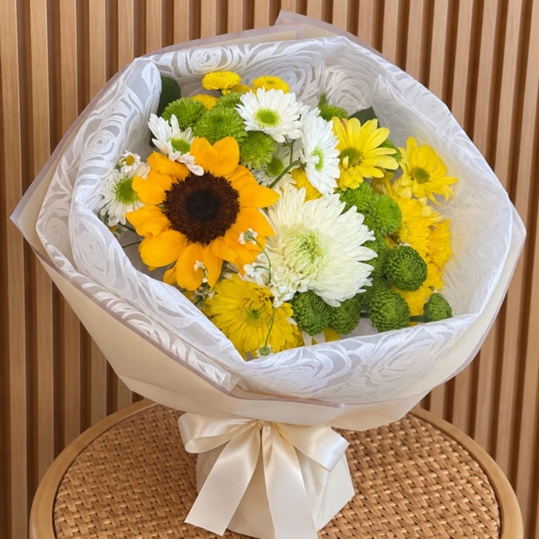 Bouquet of sunflowers, white daisies, and yellow mums wrapped in white paper