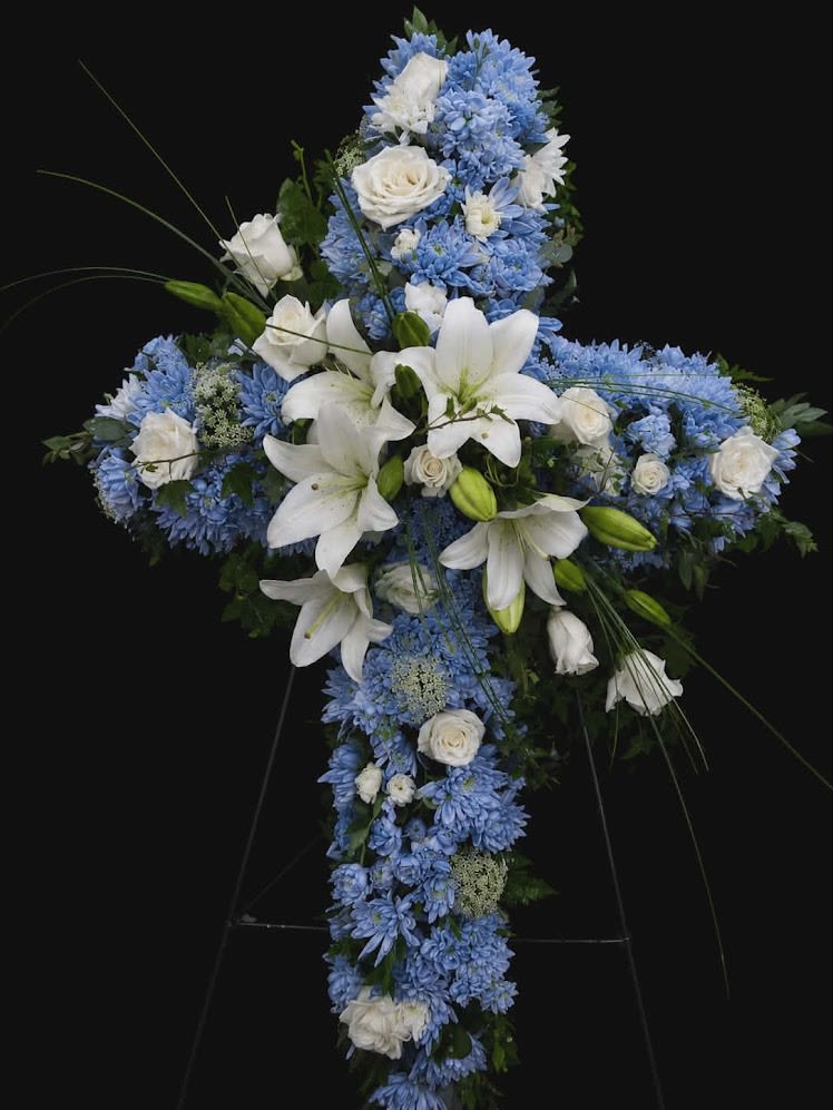 Heaven's Promise - A beautiful cross tribute featuring white lilies, roses, and soft blue blooms. Designed to honor a cherished life with faith, peace, and a heartfelt expression of love and remembrance.
