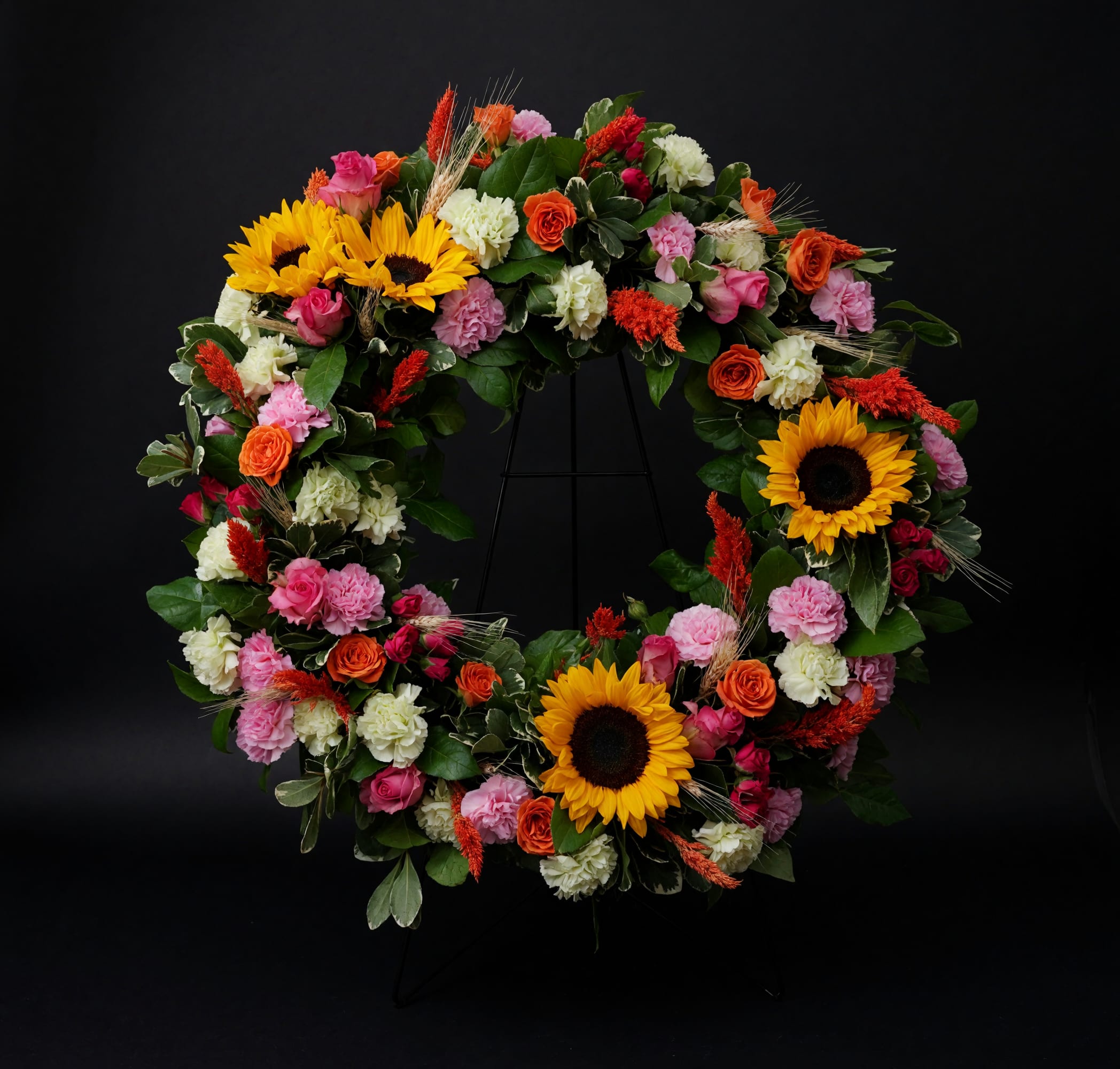 Brightest Memories - A vibrant sunflower wreath accented with roses, carnations, and seasonal blooms. 