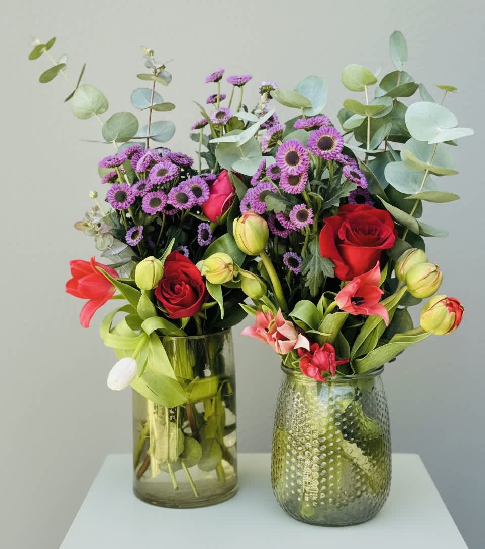 Two mixed flower arrangements in glass vases with red roses and purple blooms