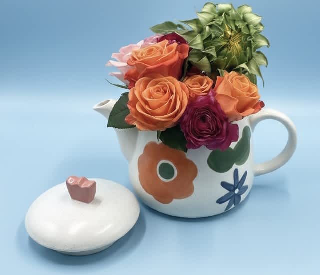 Orange and magenta roses arranged in a floral teapot with a matching lid.