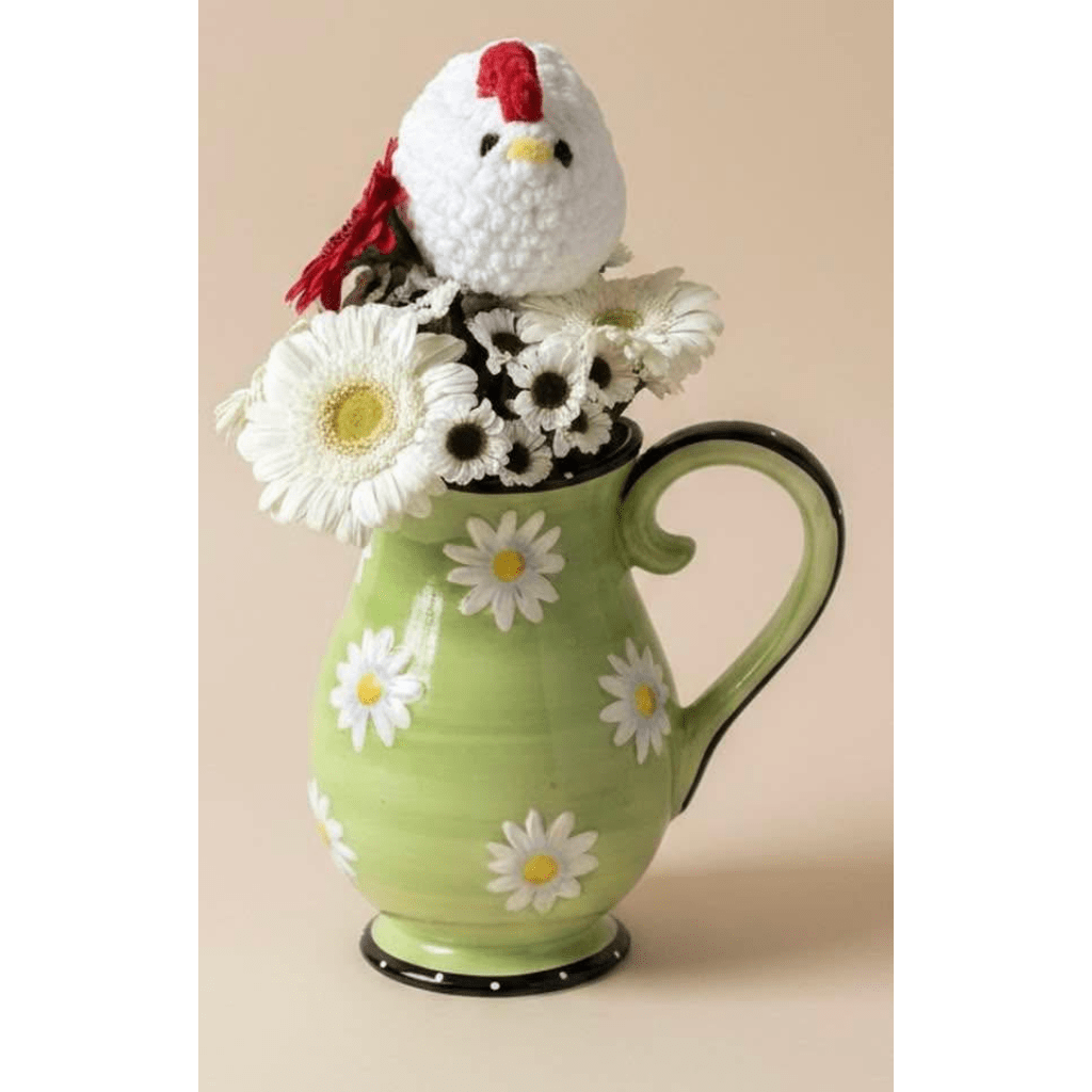 White daisies and a plush chicken sit in a green ceramic pitcher vase.