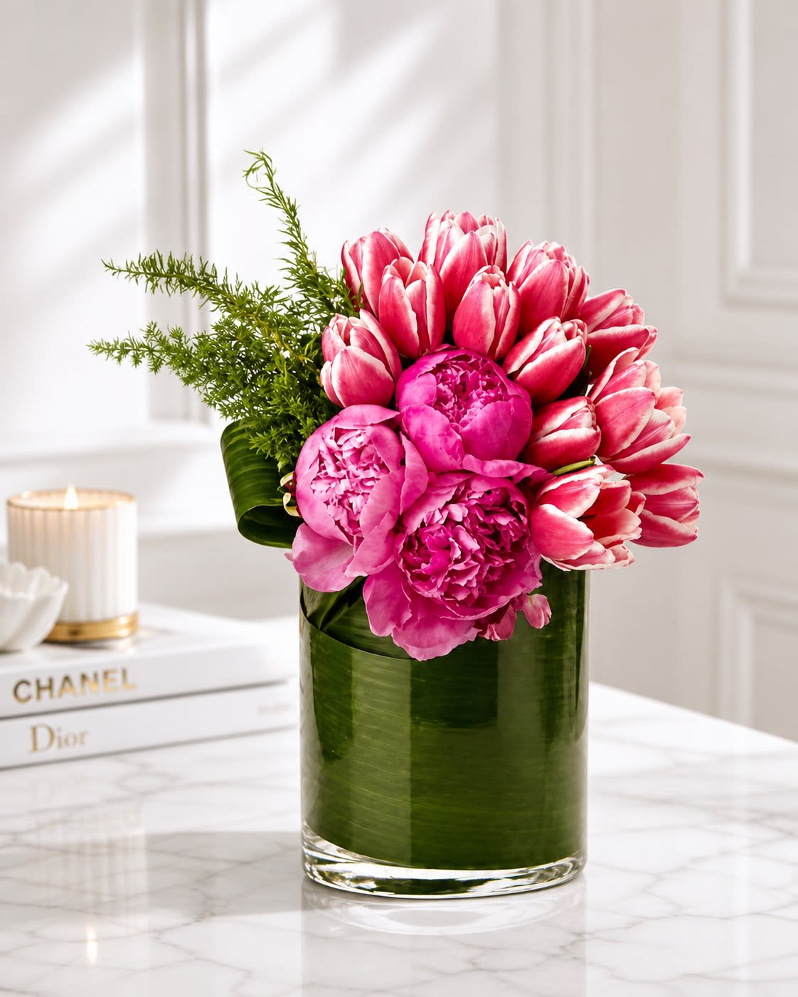 Pink Avenue - A chic garden-inspired arrangement designed with luxurious pink peonies and premium pink-and-white tulips in a modern leaf-lined cylinder vase. Pink Avenue combines soft romance with contemporary elegance, creating a fresh upscale design that feels both feminine and sophisticated. The rich layered texture of peonies paired with the graceful movement of tulips gives this arrangement a lush, high-end floral look perfect for birthdays, anniversaries, thank-you gifts, baby celebrations, or elegant home décor.  To ensure the freshest presentation possible, certain flowers or greenery may occasionally be substituted with blooms of equal or greater value while maintaining the overall pink color palette and luxurious garden style of the arrangement. Similar premium peonies, tulips, seasonal blooms, or modern greenery may be used based on availability. The vase may also vary slightly depending on inventory, but the arrangement will always be created in a comparable modern premium container that complements the overall aesthetic and value of the design.