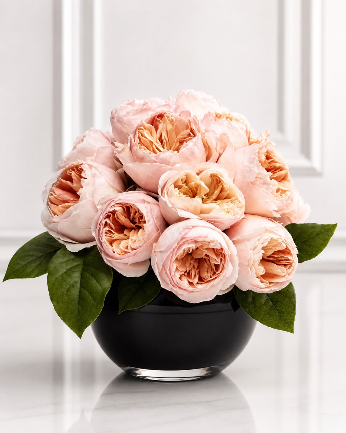 Champagne Garden Roses - An elegant luxury arrangement featuring premium garden roses in soft champagne and creamy peach tones designed in a sleek modern black glass bowl. Champagne Garden Roses is created to showcase the extraordinary layered petals and romantic texture of specialty garden roses, giving the arrangement a lush couture-inspired appearance with a timeless modern feel. The soft neutral palette paired with the dramatic black container creates a refined contrast that feels sophisticated, upscale, and effortlessly elegant.  Designed with premium seasonal garden roses and fresh greenery accents, this arrangement is ideal for anniversaries, birthdays, luxury gifting, bridal celebrations, or elevated everyday décor. Due to the specialty nature of garden roses, certain blooms or foliage may occasionally be substituted with similar luxury varieties of equal or greater value while maintaining the overall romantic aesthetic, shape, and color palette. The container may also vary slightly depending on availability, but the arrangement will always be designed in a comparable modern premium vessel that complements its luxurious style.