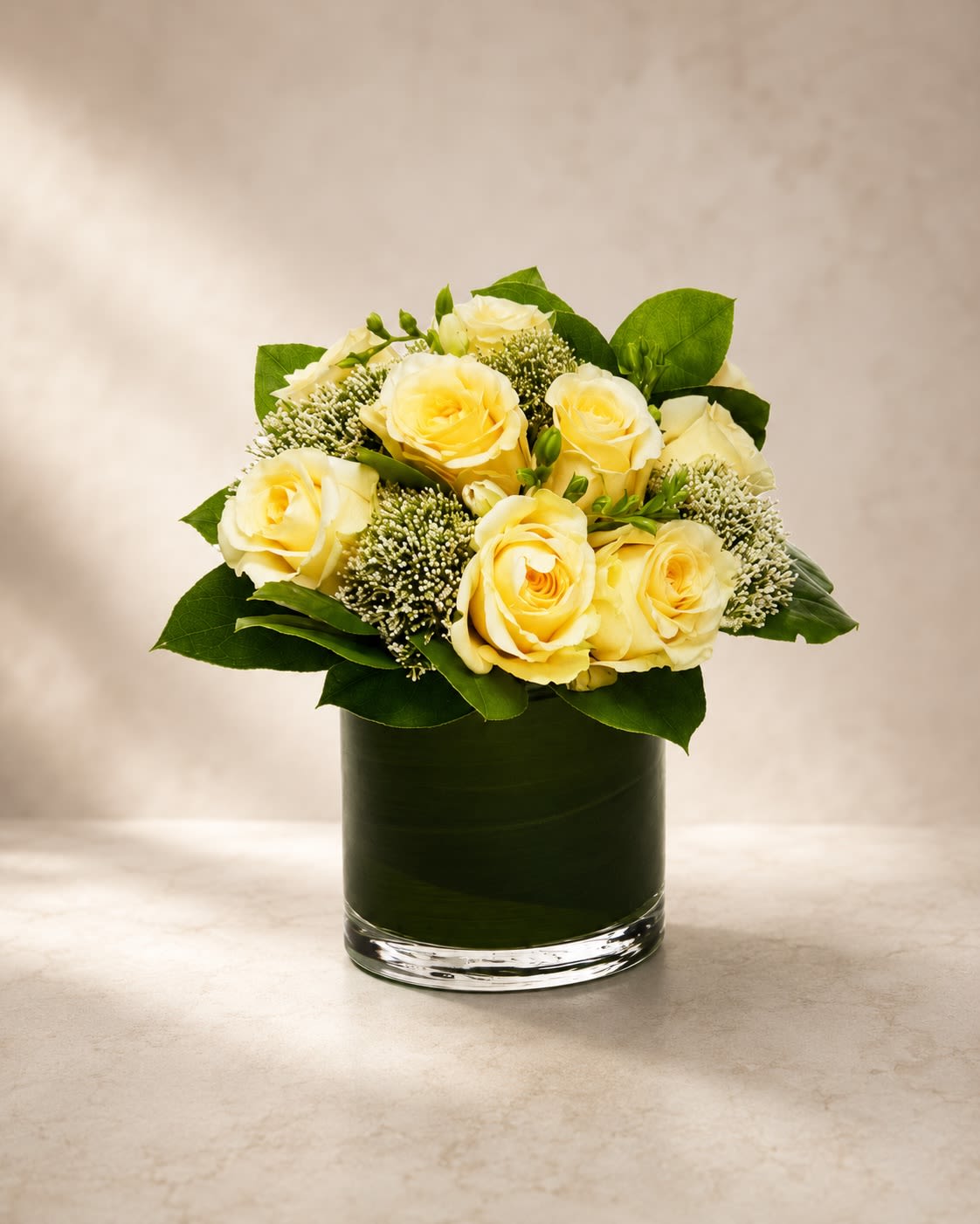 Ivory Elegance Garden - Classic, graceful, and effortlessly luxurious, Ivory Elegance Garden features creamy ivory roses accented with delicate textured fillers and lush layered greenery in a sleek modern leaf-lined vase.  Designed with timeless sophistication, this arrangement highlights the soft beauty of premium ivory roses — symbols of elegance, sincerity, peace, and refined love. The airy botanical accents add natural texture and movement, creating a fresh garden-inspired design with a modern upscale finish.  Its soft neutral palette makes this arrangement incredibly versatile and perfect for sympathy expressions, anniversaries, birthdays, thank-you gifts, corporate settings, weddings, or minimalist luxury décor.  The clean monochromatic tones paired with rich green foliage create a calming and polished presentation that feels both contemporary and timeless.