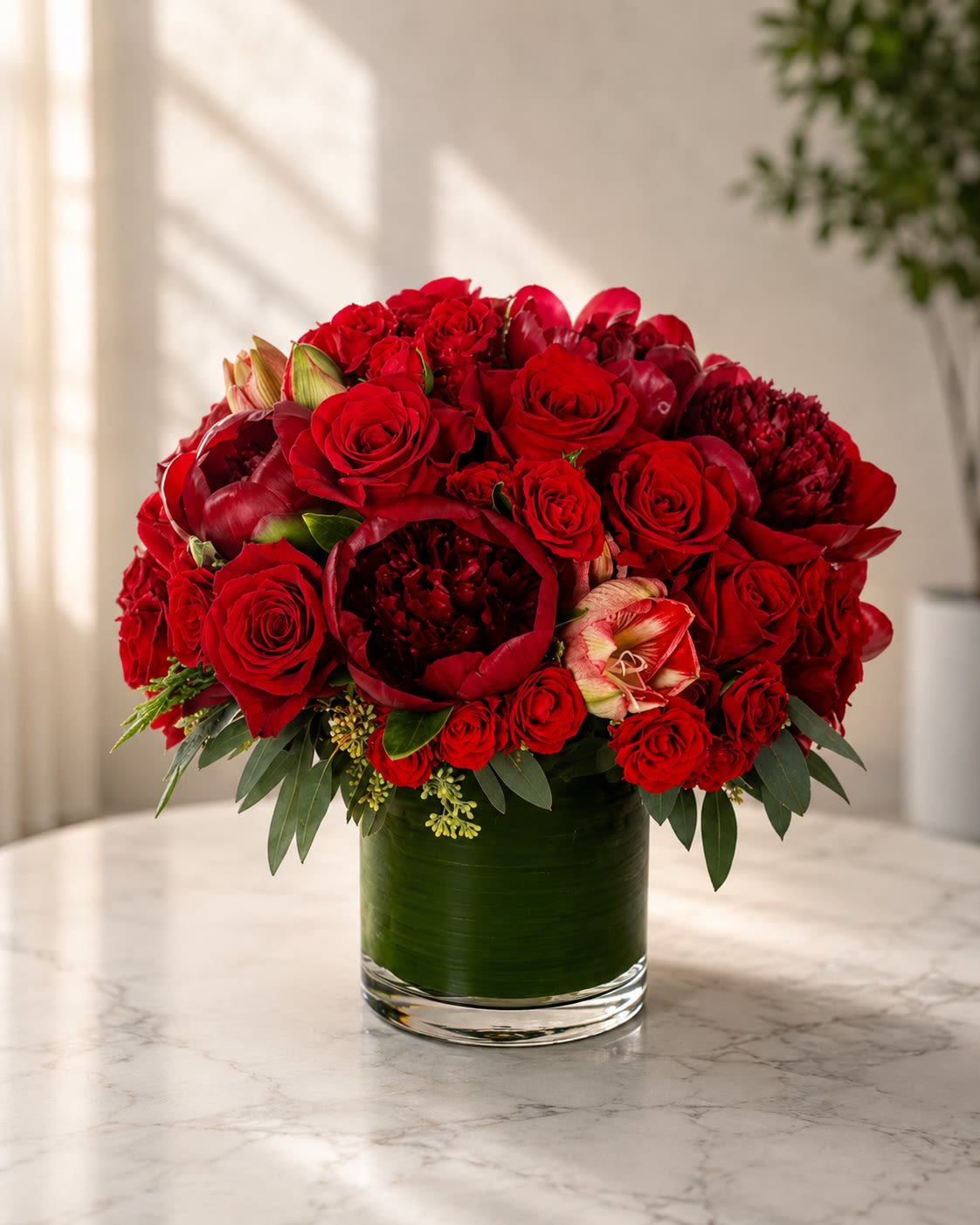 Crimson Opulence - Rich, dramatic, and exquisitely luxurious, Crimson Opulence is a breathtaking floral statement designed to embody passion, elegance, and grandeur. Overflowing with layers of premium red blooms, this couture-inspired arrangement features velvety roses, lush peonies, delicate spray roses, and specialty florals artfully composed in a modern leaf-lined glass vase.  The monochromatic crimson palette creates a bold and sophisticated presence while the layered textures add depth, romance, and refinement. Inspired by luxury floral ateliers and high-end editorial styling, this arrangement feels timeless yet powerfully modern.  Perfect for anniversaries, romantic celebrations, luxury gifting, Valentine’s Day, upscale events, or unforgettable grand gestures, Crimson Opulence was designed to leave a lasting impression.