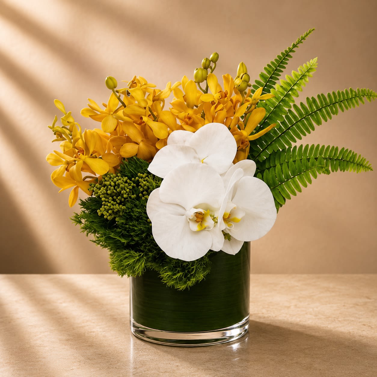 Golden Eden - Elegant, tropical, and effortlessly refined, Golden Eden is a luxurious designer arrangement featuring radiant golden mokara orchids paired with pristine white phalaenopsis orchids, lush textural greenery, and sculptural tropical foliage in a sleek modern vase.  The contrast between vibrant gold and crisp white creates a striking balance of warmth and sophistication. The layered orchids give the arrangement a couture botanical feel while the dramatic fern accents add movement and architectural elegance.  Inspired by upscale tropical resorts and modern luxury interiors, this arrangement is designed to feel serene, exotic, and unforgettable.
