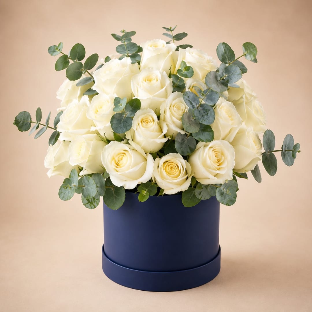 White roses arranged in a navy round box with eucalyptus