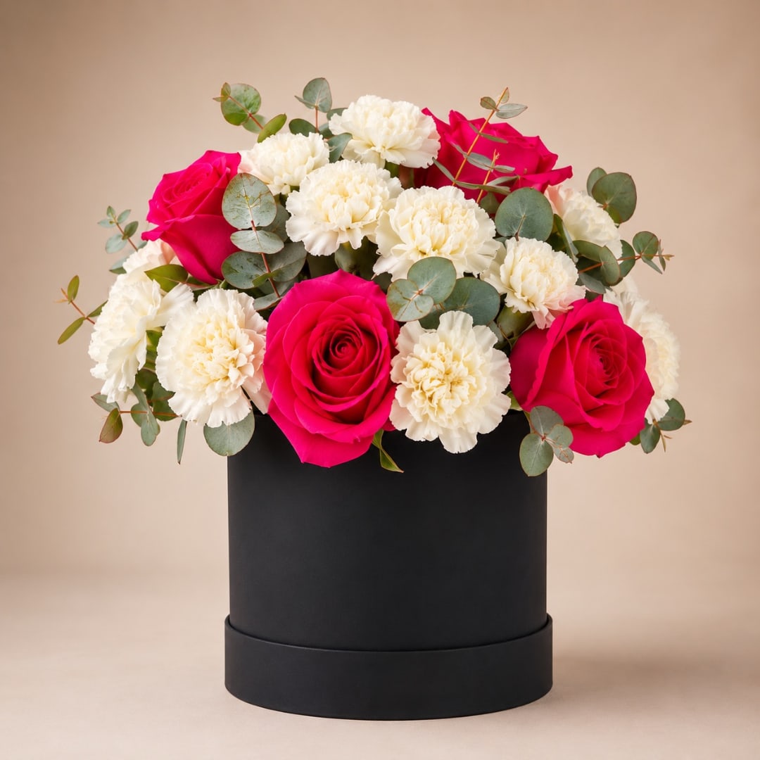 Pink roses and white carnations arranged in a black hat box