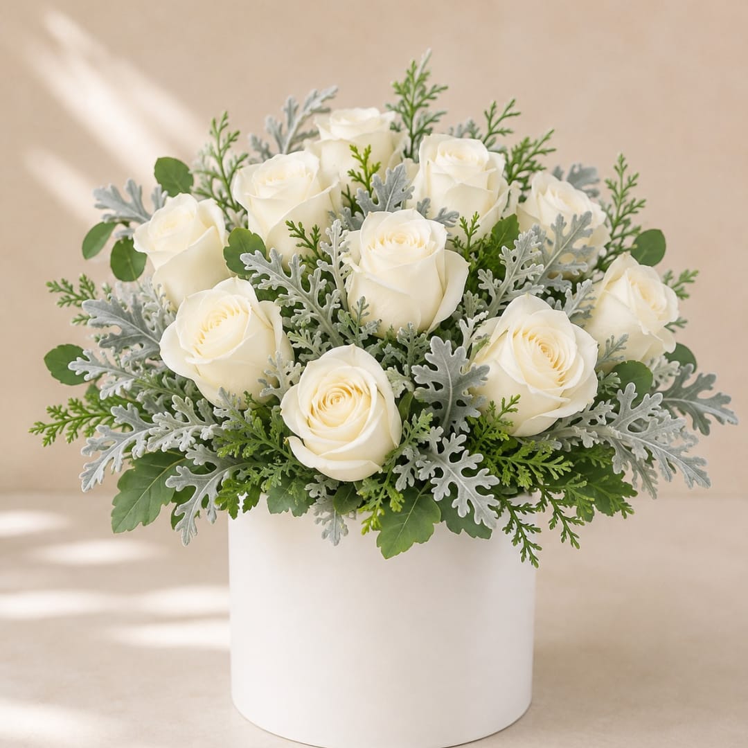 White roses arranged in a white cylindrical vase with silver-green foliage