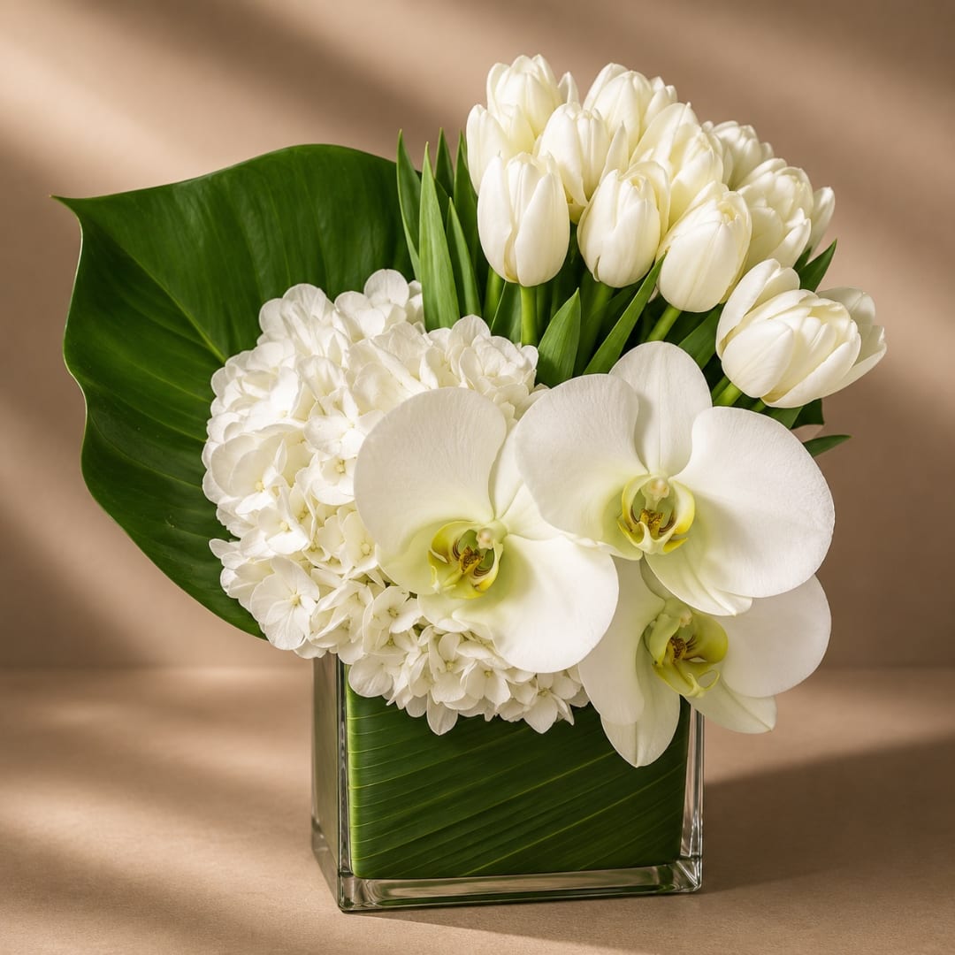 White tulips, hydrangea, and orchids arranged in a glass vase