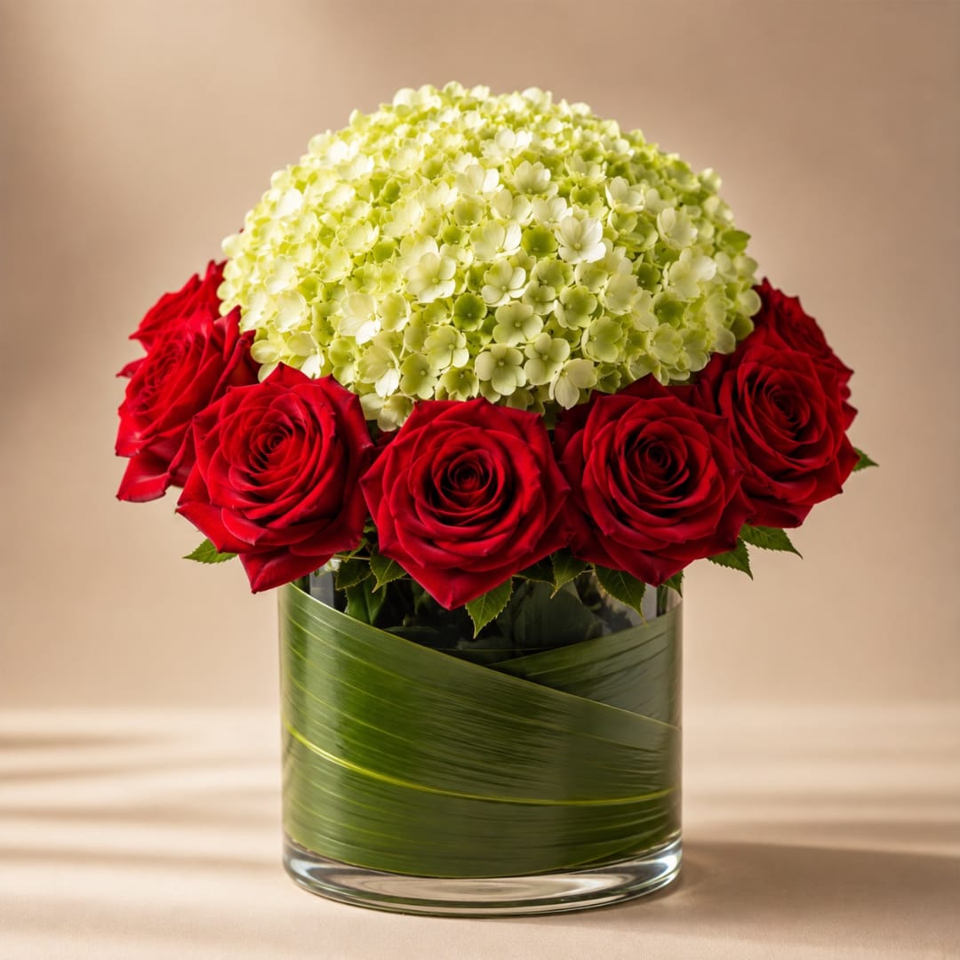 Red roses arranged around a pale green hydrangea dome in a glass vase