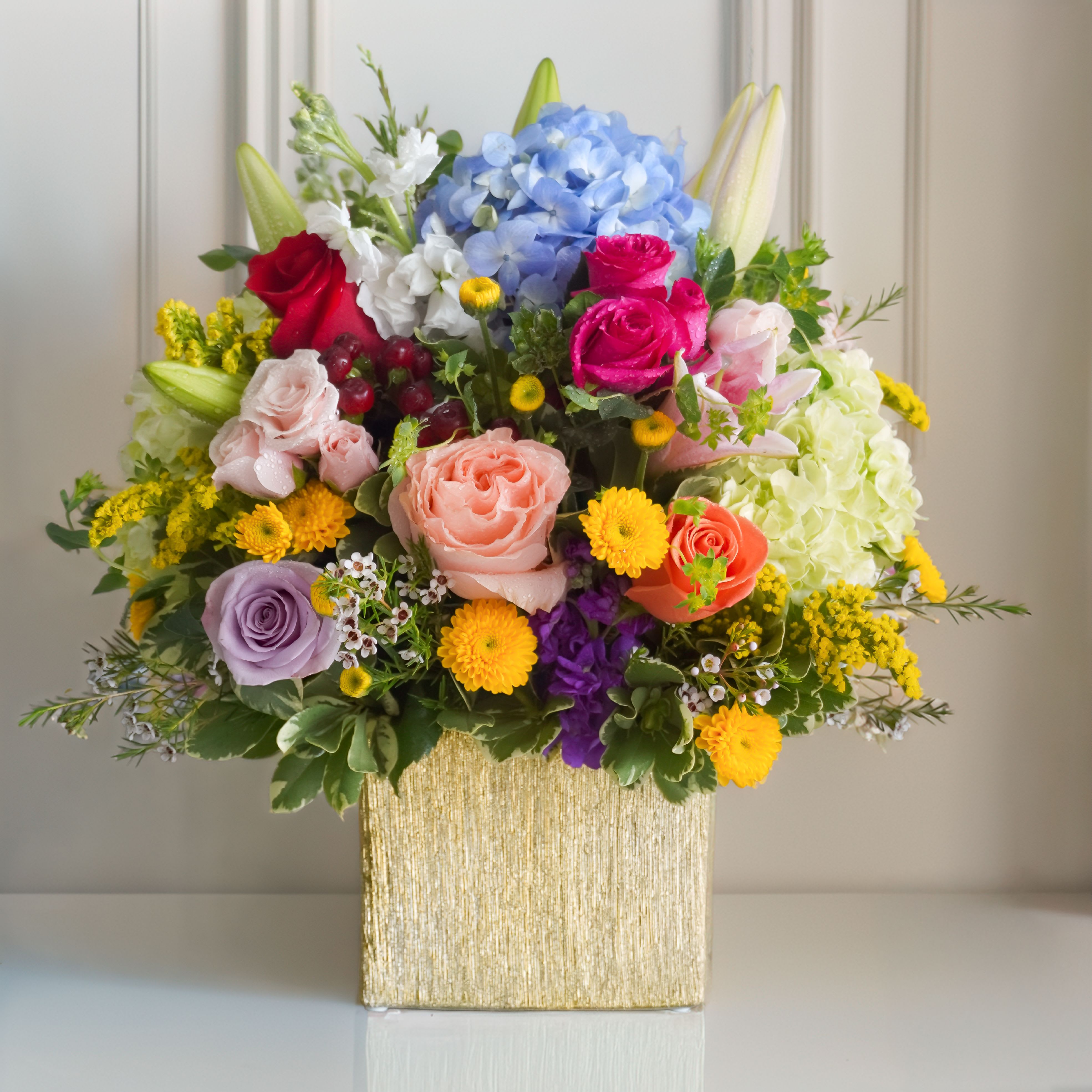 Best Day Bouquet by Atlanta's Finest Flowers  - A large blue hydrangea anchors a joyful, garden-style mixed bouquet that reads like a celebration in bloom - perfect as a birthday bouquet, Mother's Day gift, or a bright "just because" surprise for someone who deserves to feel seen. The Best Day Bouquet by Atlanta's Finest Flowers pairs jewel and pastel tones - pink, lavender, coral, white, yellow and blue - to create an uplifting arrangement that also works beautifully for get well wishes, thank yous, or congrats moments.  This full, layered design features hydrangeas, roses, spray roses, lilies, alstroemeria and chrysanthemums with soft white filler accents for texture and movement. Tall white lilies rise above the composition while clusters of small yellow daisy-like blooms add pops of sunshine around the edges. The bouquet arrives arranged in a tasteful gold square vase (6x6 gold cube), giving it a decorative, gift-ready presence that suits spring gatherings, anniversaries, or a thoughtful desk or home display.  Choose this arrangement for the person who loves color and classic garden charm - she'll feel genuinely celebrated whether it's Women's Day, Best Friends Day, or a simple pick-me-up. Available in the pictured gold cube vase, it ships ready to display; fresh-cut stems respond well to regular water changes and a clean vase to keep blooms vibrant longer.
