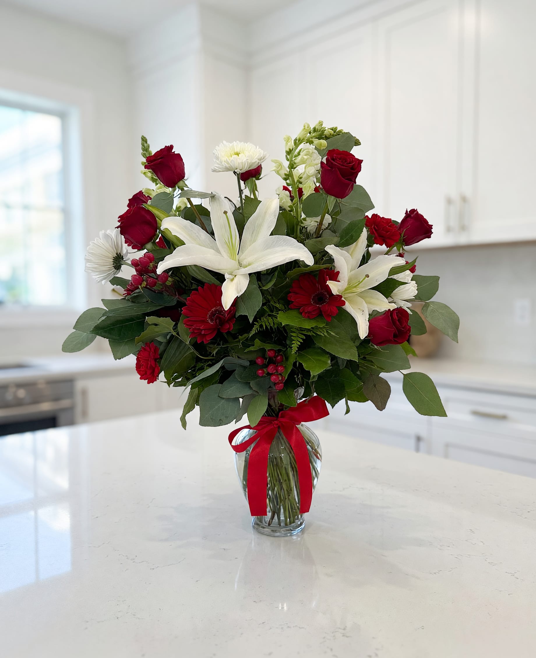 Bouquet of red roses and white lilies in a glass vase with a red ribbon