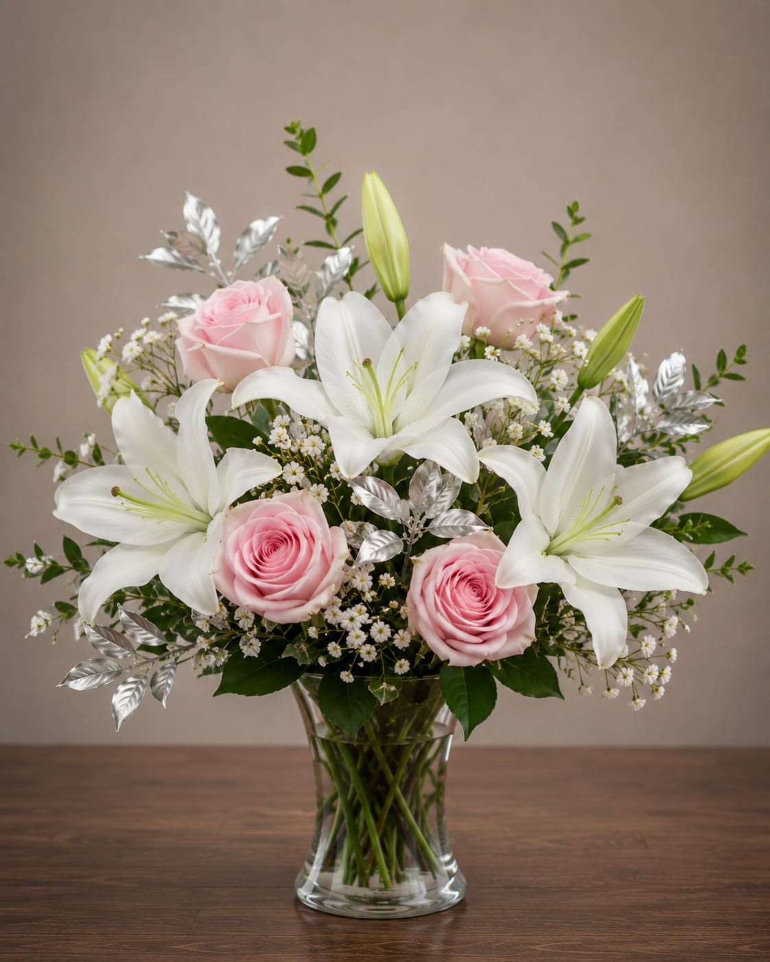 Sweet Serenity - A calm, elegant mix of white lilies and soft pink roses arranged in a clear glass vase-this flower arrangement is perfect as a sympathy arrangement, anniversary roses gift, or a thoughtful everyday bouquet to let someone know you're thinking of them. The lilies give graceful height while the rounded clusters of roses create a romantic focal point, so the recipient will feel comforted and cherished the moment it arrives.  Carefully balanced with small white filler flowers and silver-toned foliage for subtle texture, the palette of white, pink and green keeps the look fresh and polished. The design is full without feeling fussy, presented in a clear glass vase that showcases the stems and reads as classic mixed-flower styling. Ideal for spring celebrations, a bedside or dining table centerpiece, or as a gentle surprise-arrangement dimensions and vase details are included at checkout; keep blooms in fresh water and away from direct heat to extend their life.