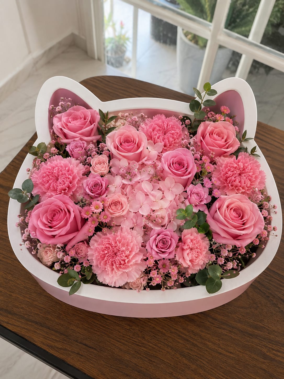 Kitty's Garden - A dense cluster of pink roses, carnations, and pale pink hydrangeas arranged inside a whimsical cat-shaped gift box makes this flower arrangement an instant smile-giver-perfect as a birthday bouquet, a Mother's Day surprise, or a romantic gesture. The playful silhouette of the box and the soft pink palette create a sweet, feminine presence that will make the person you're thinking of feel cherished and noticed.  Creamy pink roses and ruffled carnations mingle with cushiony hydrangea blooms, while small daisy-like filler flowers and sprigs of greenery add delicate texture and a light, garden-fresh look. The white-edged cat box frames the arrangement for an easy tabletop display; size and stem length are tailored to fit the box for immediate enjoyment with minimal fuss.  Made to be an everyday delight, this arrangement suits anyone who loves charming, compact floral gifts-moms, partners, or friends who appreciate cute details. No vase needed: simply place on a shelf or table, keep the floral foam moist, and refresh with a little water to extend enjoyment.