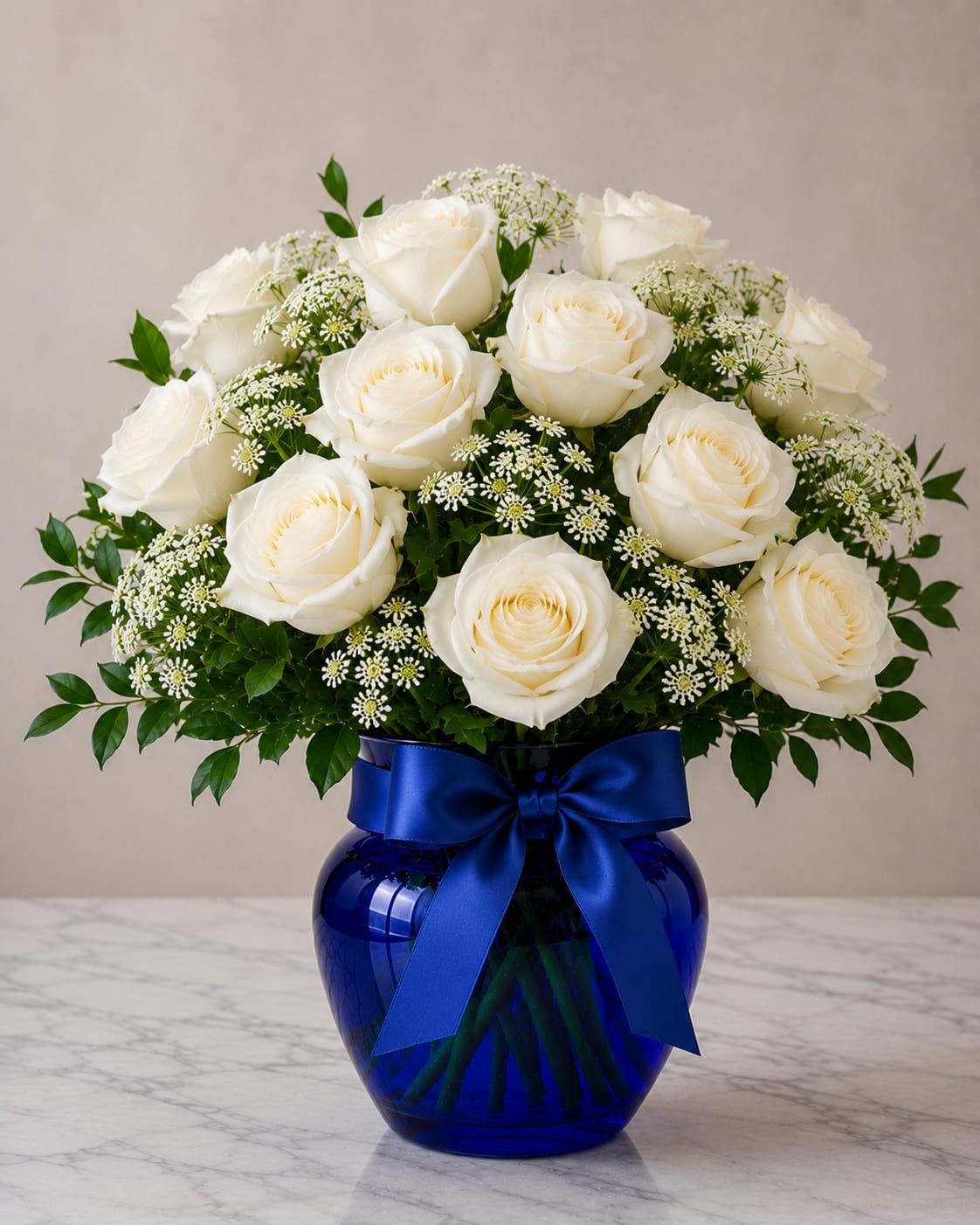 White roses arranged in a blue glass vase with a ribbon