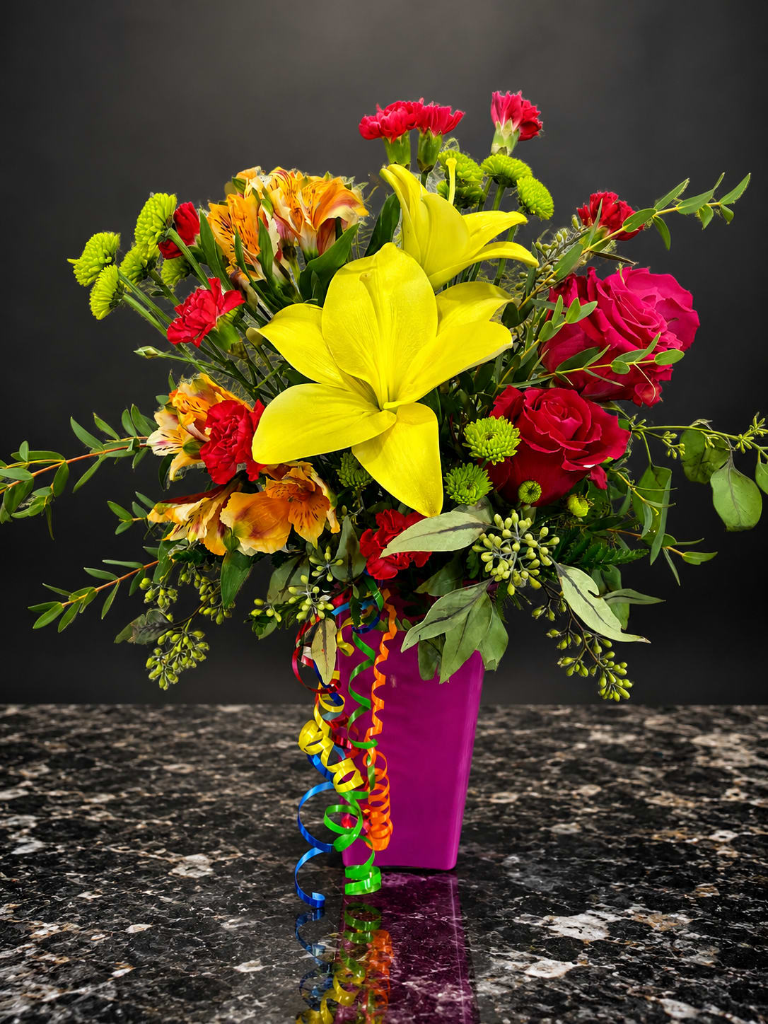 Bright mixed bouquet with yellow lilies, red roses, and a magenta vase