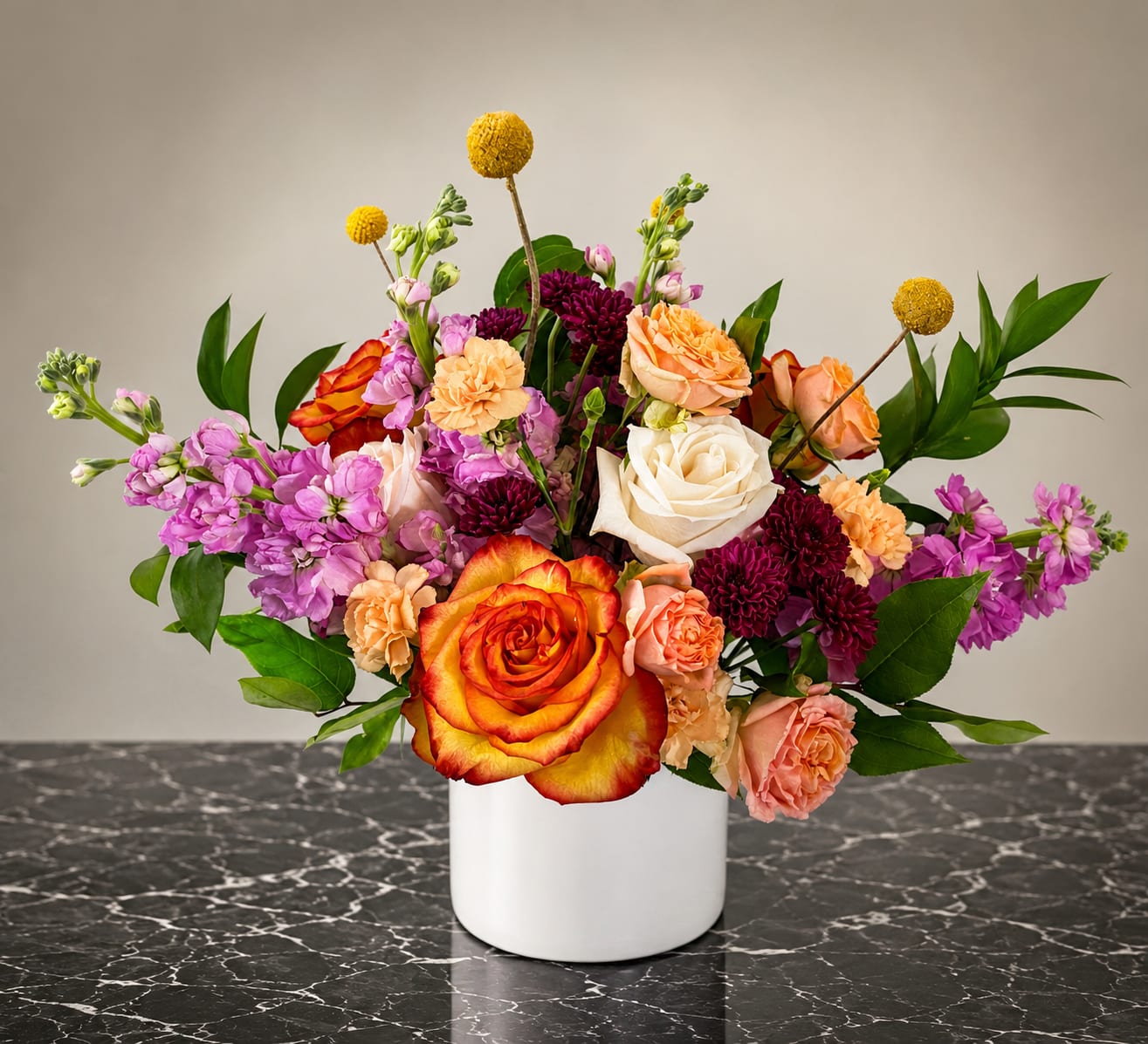 Mixed bouquet of roses, carnations, and purple blooms in a white vase