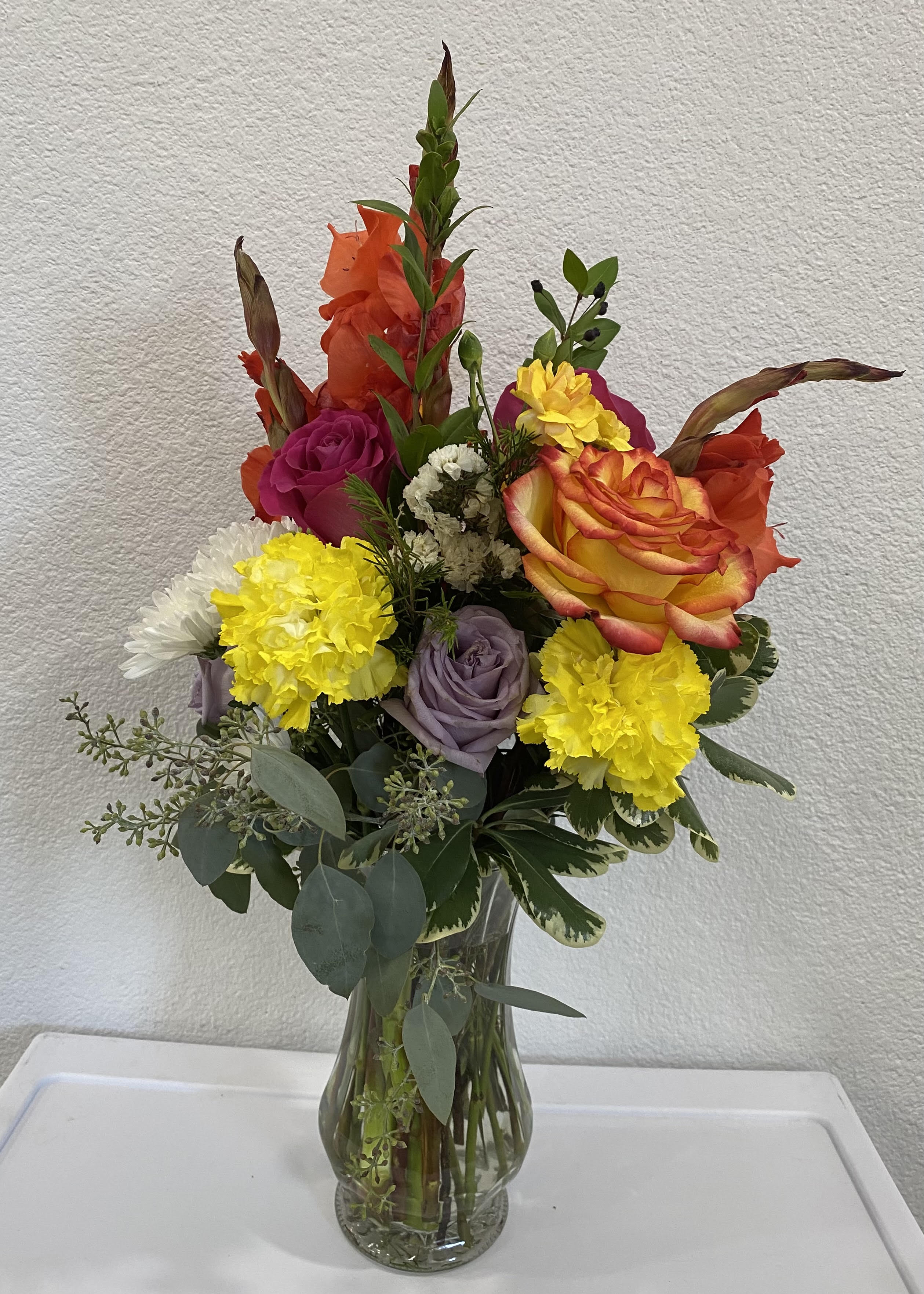 Mixed bouquet in a clear glass vase with roses, carnations, and daisies