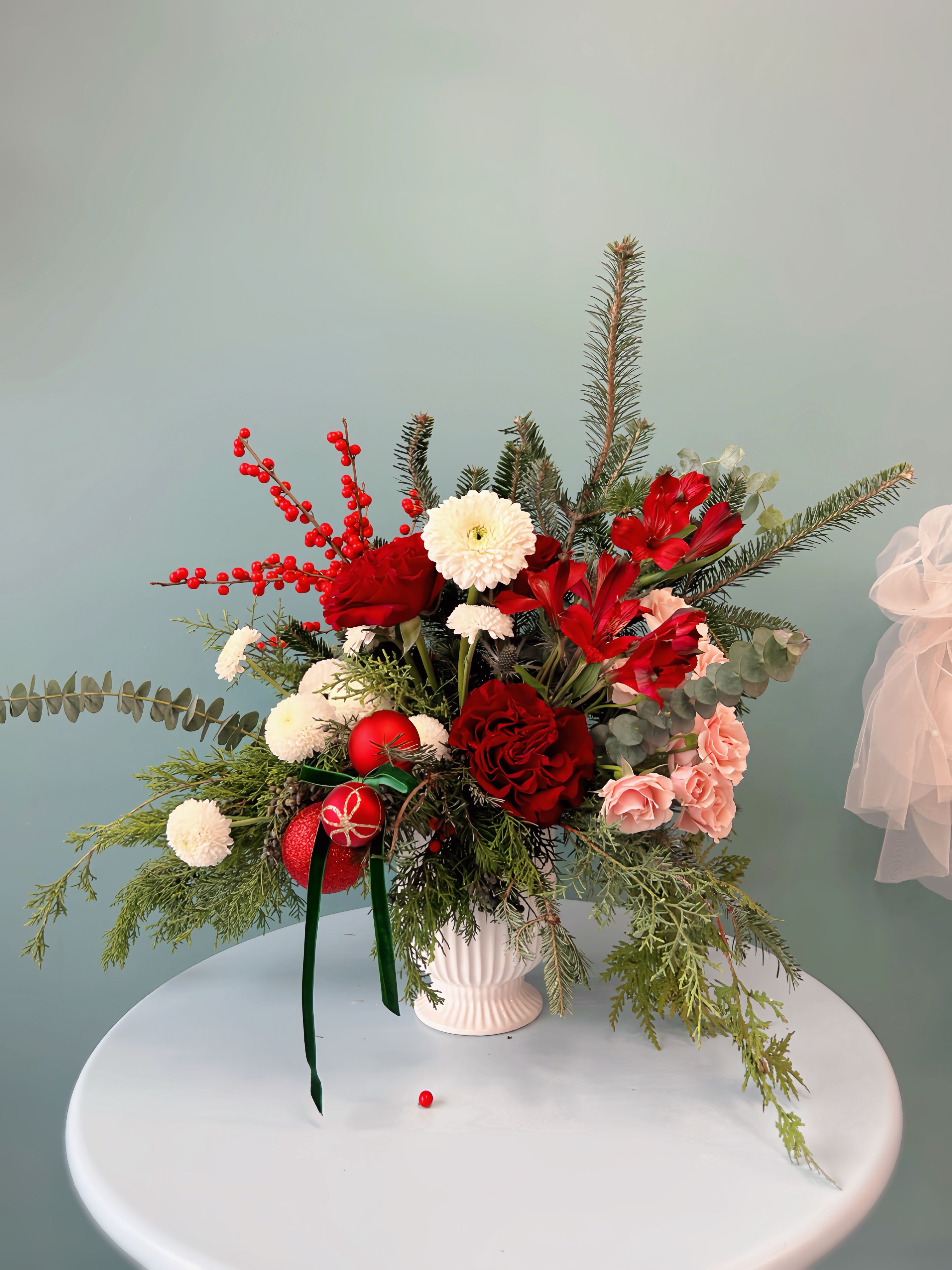 "Velvety Elegance "  Winter Collection  - Add a touch of classic holiday sophistication to your table with the Timeless Holiday Elegance Centerpiece, available in Standard, Deluxe, and Premium sizes. Each centerpiece is crafted with a luxurious mix of premium roses and amaryllis, charming alstroemeria and sprigs of ilex berries, beautifully complemented by lush winter greens like cedar and pine. Accented with velvet ribbon, this arrangement captures the spirit of the season with a timeless, festive charm.  Standard: Perfect for smaller gatherings, with essential premium florals to add elegance to any space.  Deluxe: A fuller arrangement featuring additional seasonal blooms, ideal for a central display on a holiday table.  Premium: A grand version with extra florals and decorative touches for a stunning, unforgettable holiday centerpiece