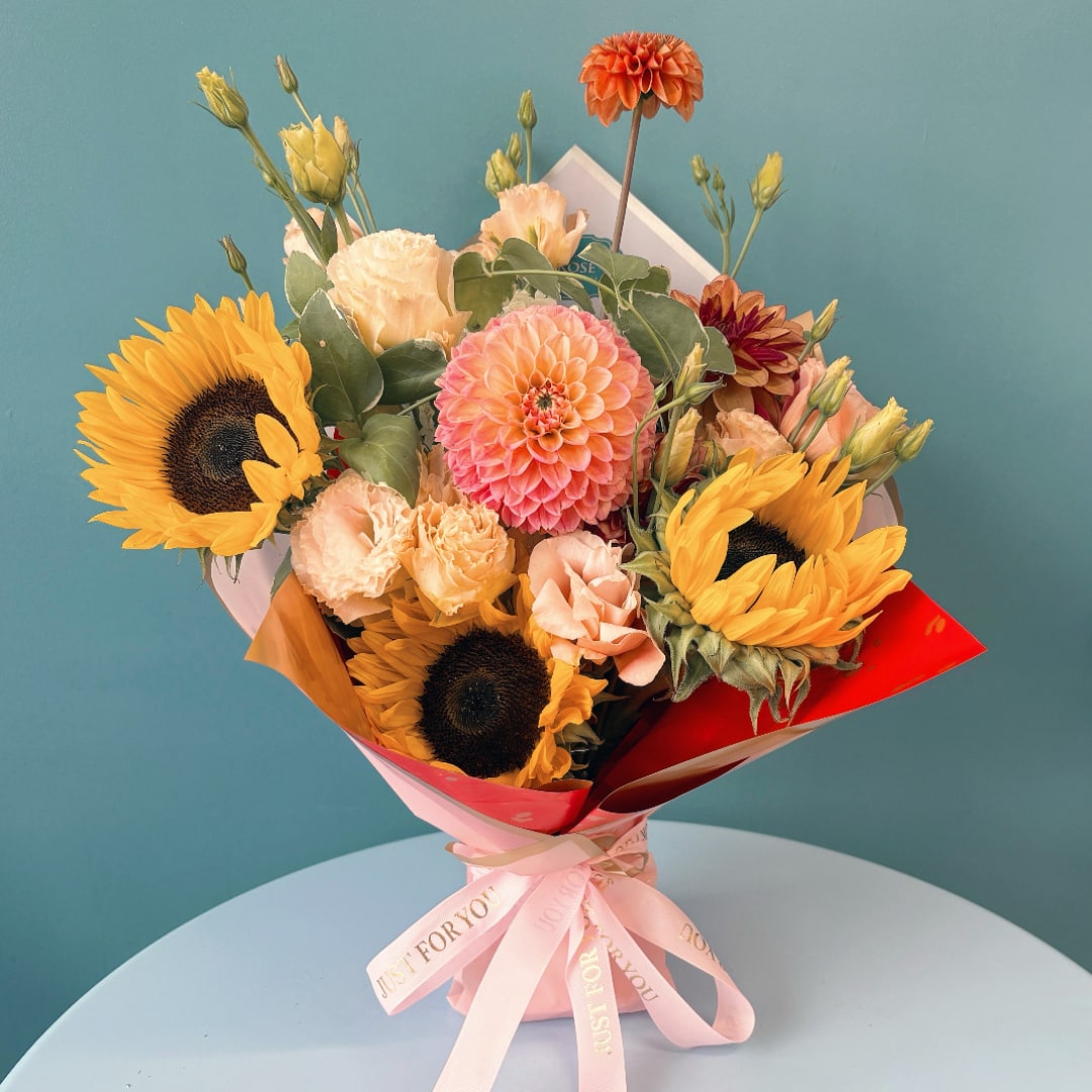 Bouquet of sunflowers, dahlias, and peach flowers wrapped in pink paper