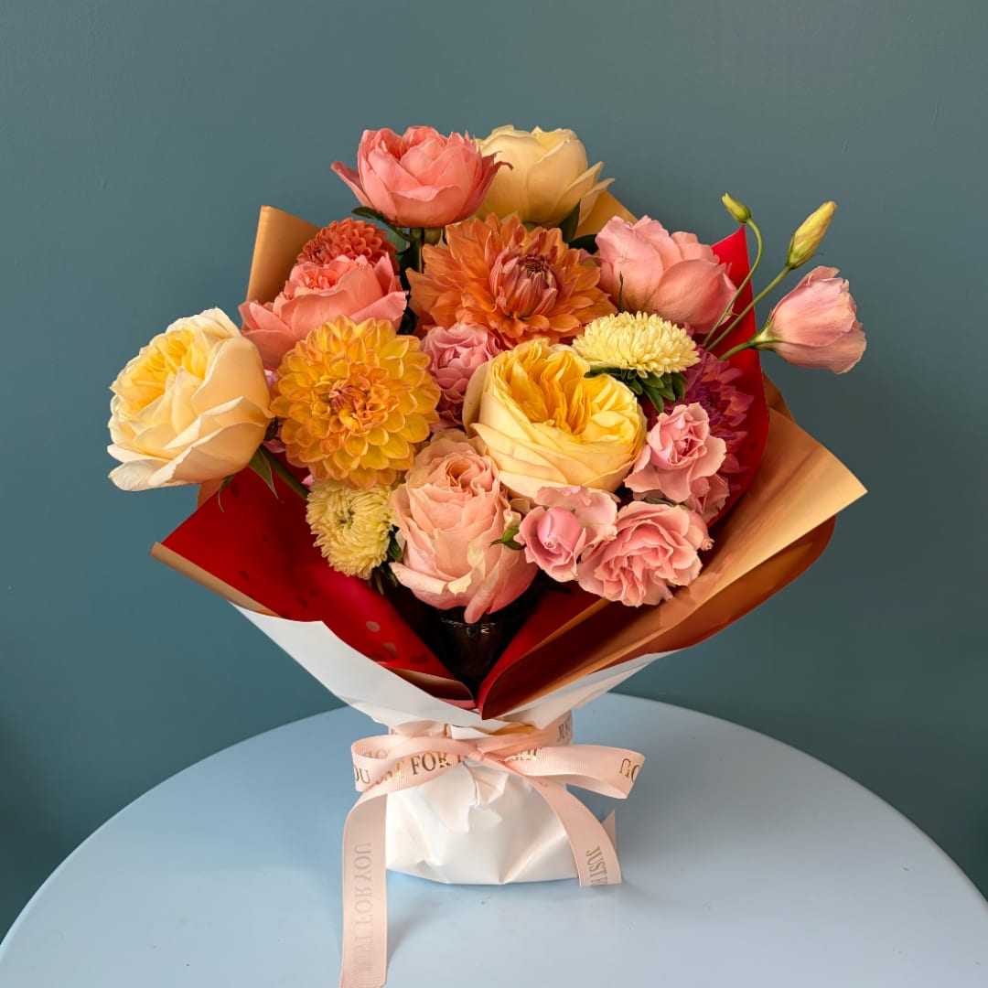 Bouquet of pink, peach, and yellow flowers wrapped in red and tan paper