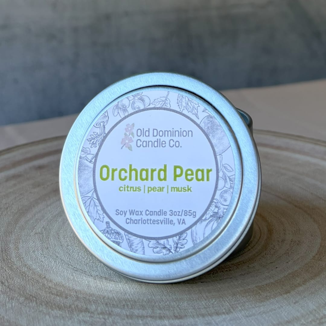 Small tin candle labeled Orchard Pear on a wooden surface