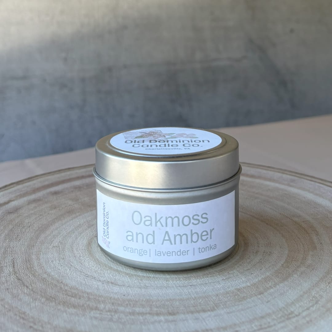 A small tin candle labeled Oakmoss and Amber on a wooden tray