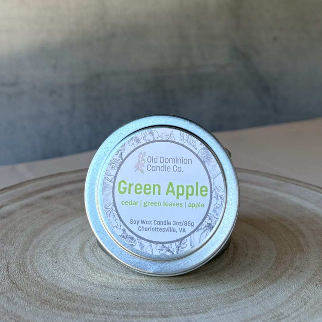 Small tin candle labeled Green Apple on a wooden surface