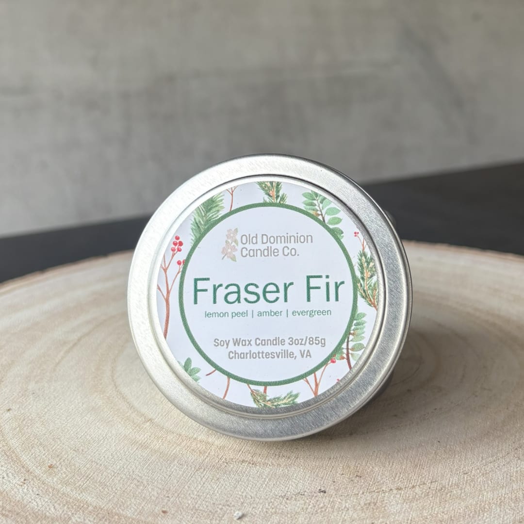 Small tin candle labeled Fraser Fir on a wooden surface