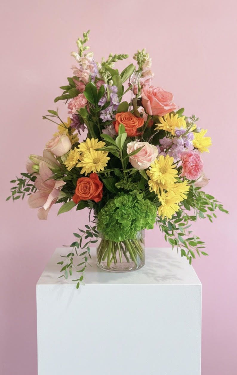 My Precious - A tall, airy bouquet of pink and orange roses with cheerful yellow daisy-like blooms and pastel snapdragons-perfect as a birthday bouquet or a thoughtful everyday gift that makes someone feel truly cherished. My Precious reads as light and garden-fresh: blooms rise above a clear glass vase in a loose, layered composition that feels lively without being fussy, so the person you're thinking of will feel celebrated and seen.  This arrangement pairs soft pink and coral roses with sunny yellow daisies, lilac-tinted snapdragons, trailing greenery, and other seasonal stems for texture and movement. Displayed in a clear glass vase, the design stands tall (flowers extend above the vase) and measures as a generous, loose garden-style arrangement that fills a room with color and soft, romantic energy.  Ideal for anniversaries, birthdays, or "just because" moments when you want to brighten someone's day, My Precious sends a cheerful, feminine message. Care is simple: keep water fresh and trim stems every few days to maintain the arrangement's airy shape and extend its lively, long-lasting presence.