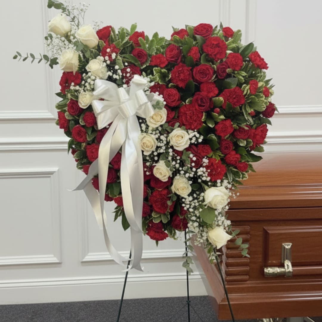 Heart-shaped red and white rose spray on an easel beside a casket