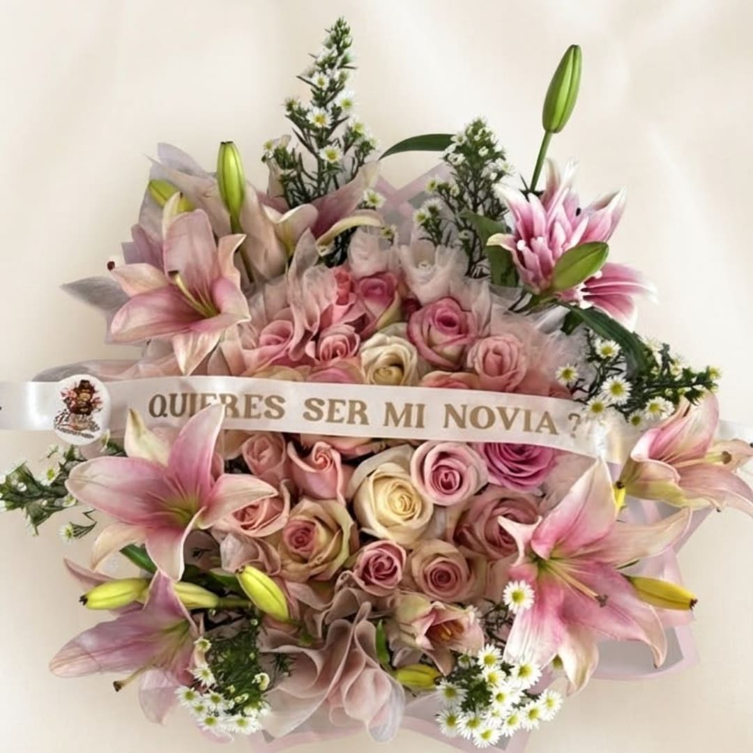 Pink lilies and roses arranged with a ribbon reading "Quieres ser mi novia?"