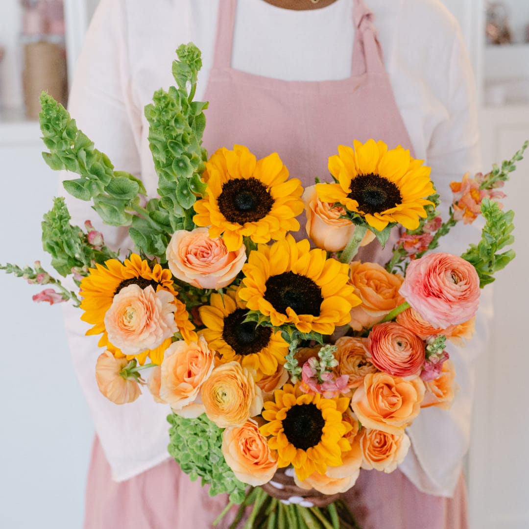 Bouquet of sunflowers, peach roses, and ranunculus held by a person