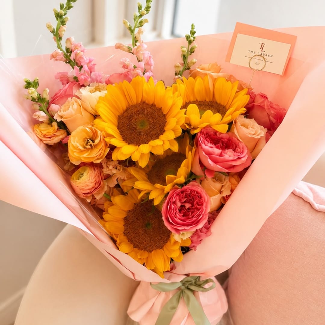 Bouquet of sunflowers, roses, and pink snapdragons wrapped in peach paper