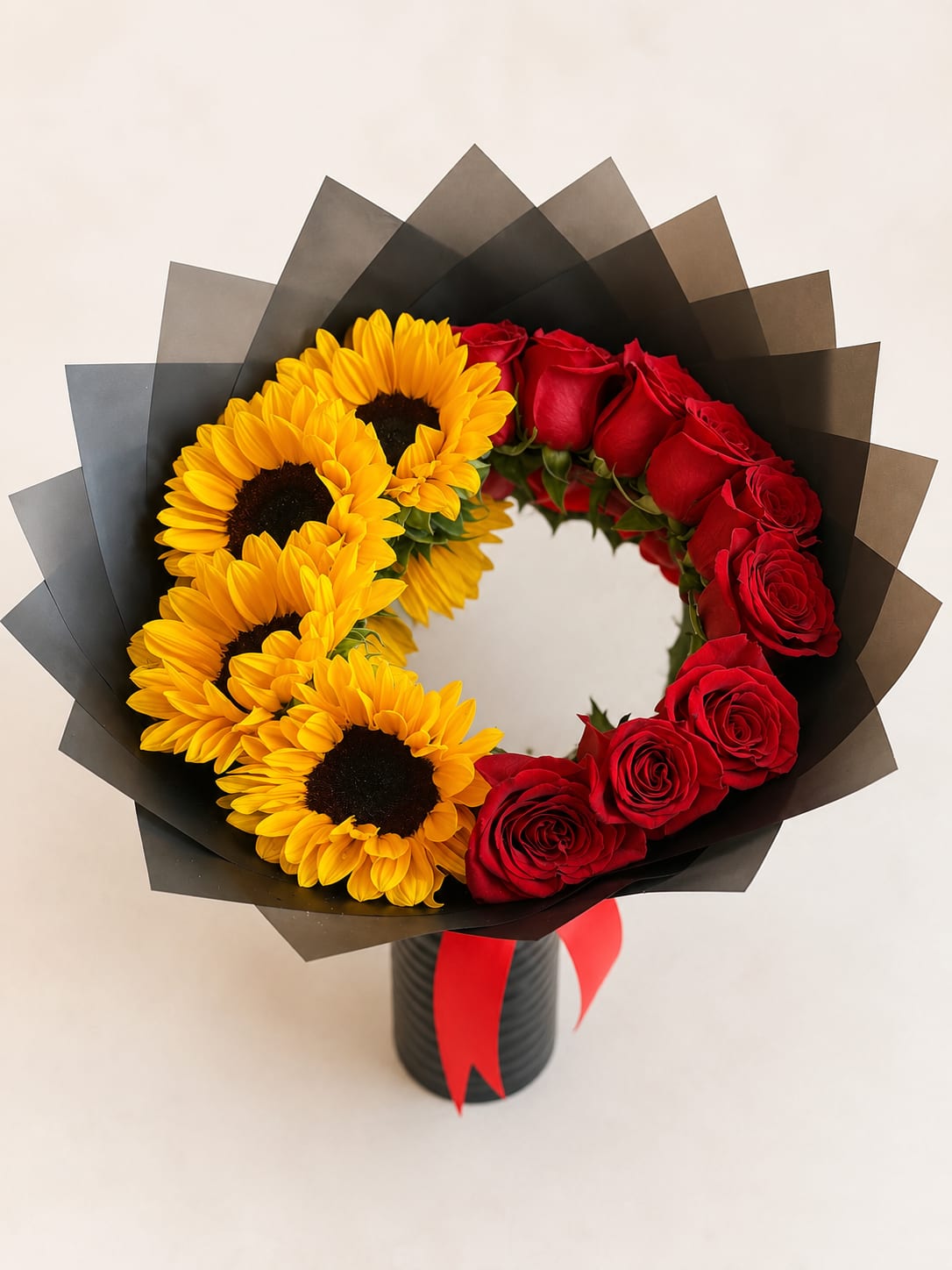 Bouquet of red roses and yellow sunflowers in black wrap with a red ribbon