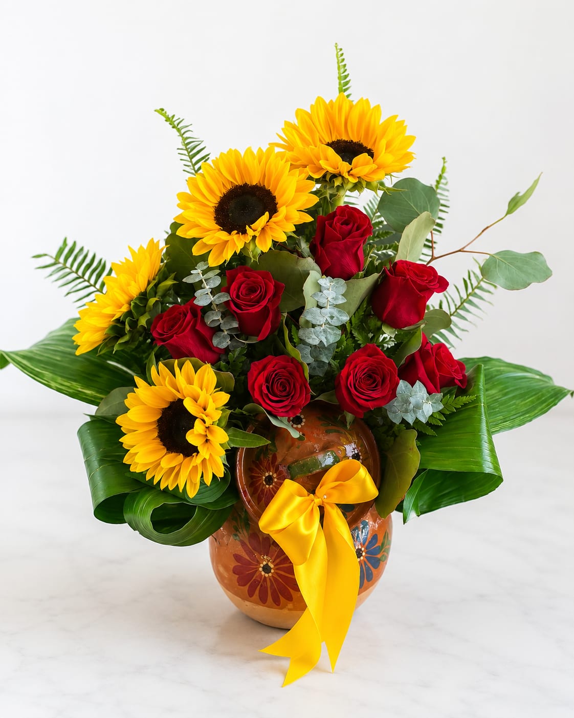 Bouquet of red roses and yellow sunflowers in a painted vase with a yellow ribbon