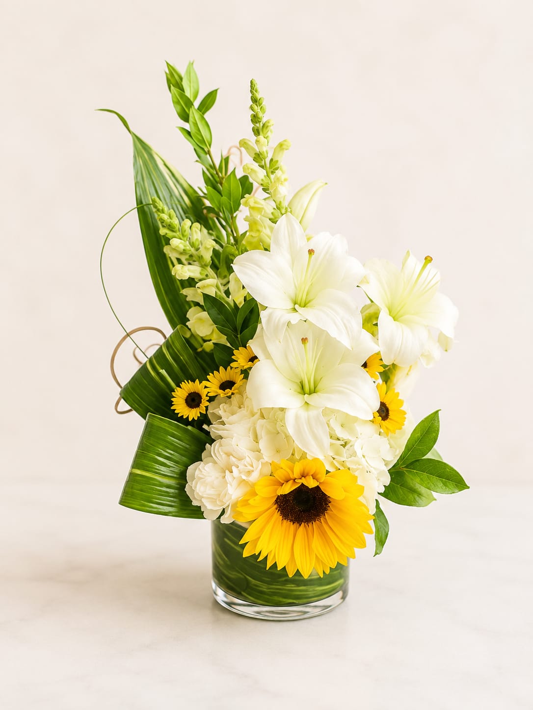 White lilies and yellow sunflowers in a glass vase