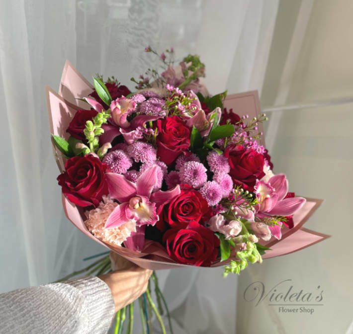 Handheld bouquet of red roses and pink orchids wrapped in blush paper