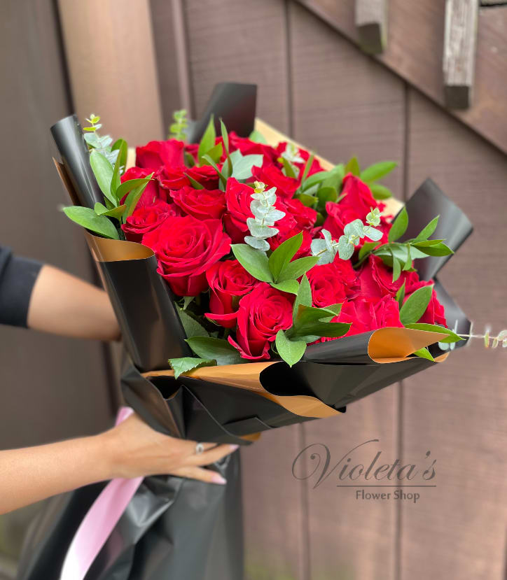Bouquet of red roses wrapped in black paper with green foliage
