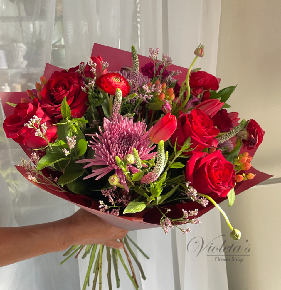 Handheld bouquet of red roses and pink mixed flowers wrapped in burgundy paper