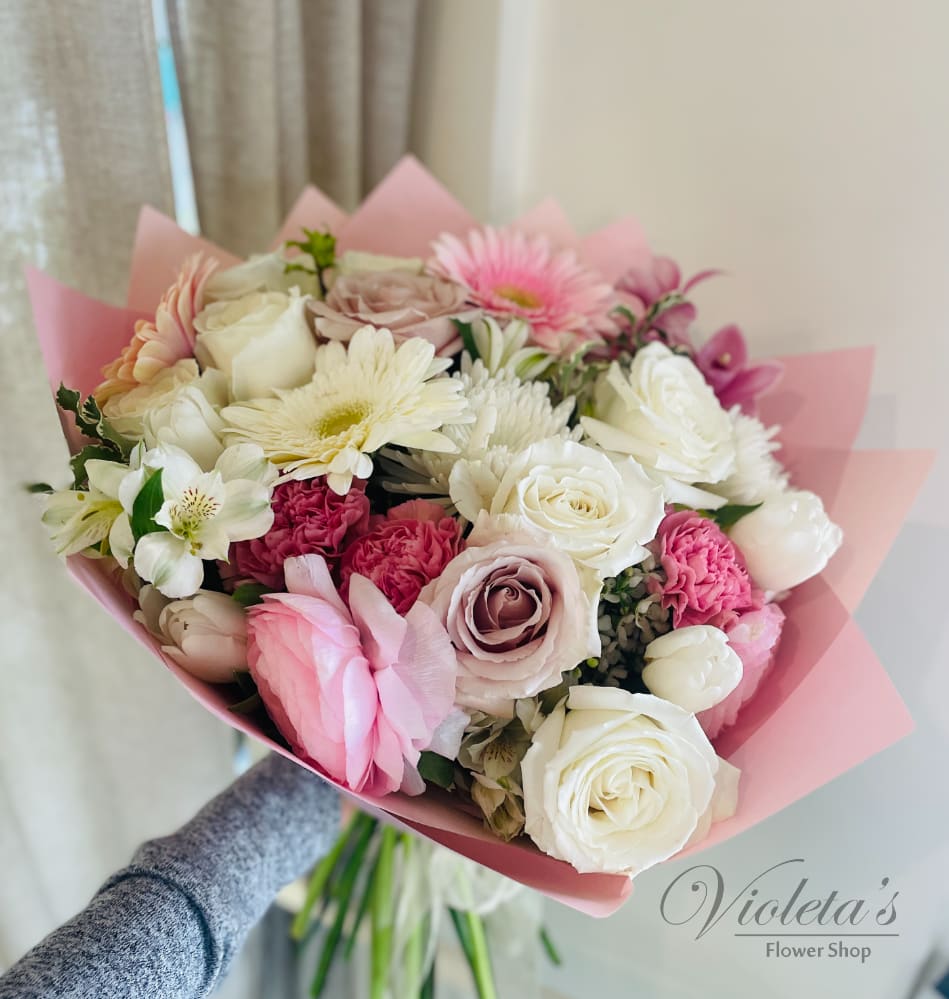 Handheld bouquet of pink and white roses with mixed blooms wrapped in pink paper