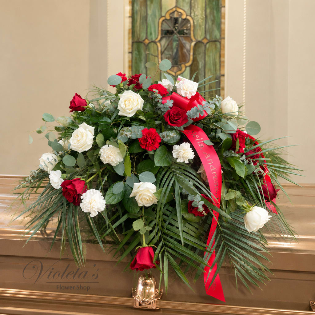 Red and white roses arranged in a casket spray with a red ribbon