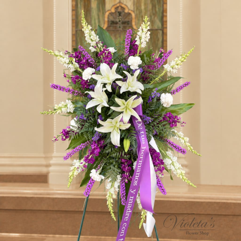 Standing floral spray with white lilies and purple flowers on a ribboned easel